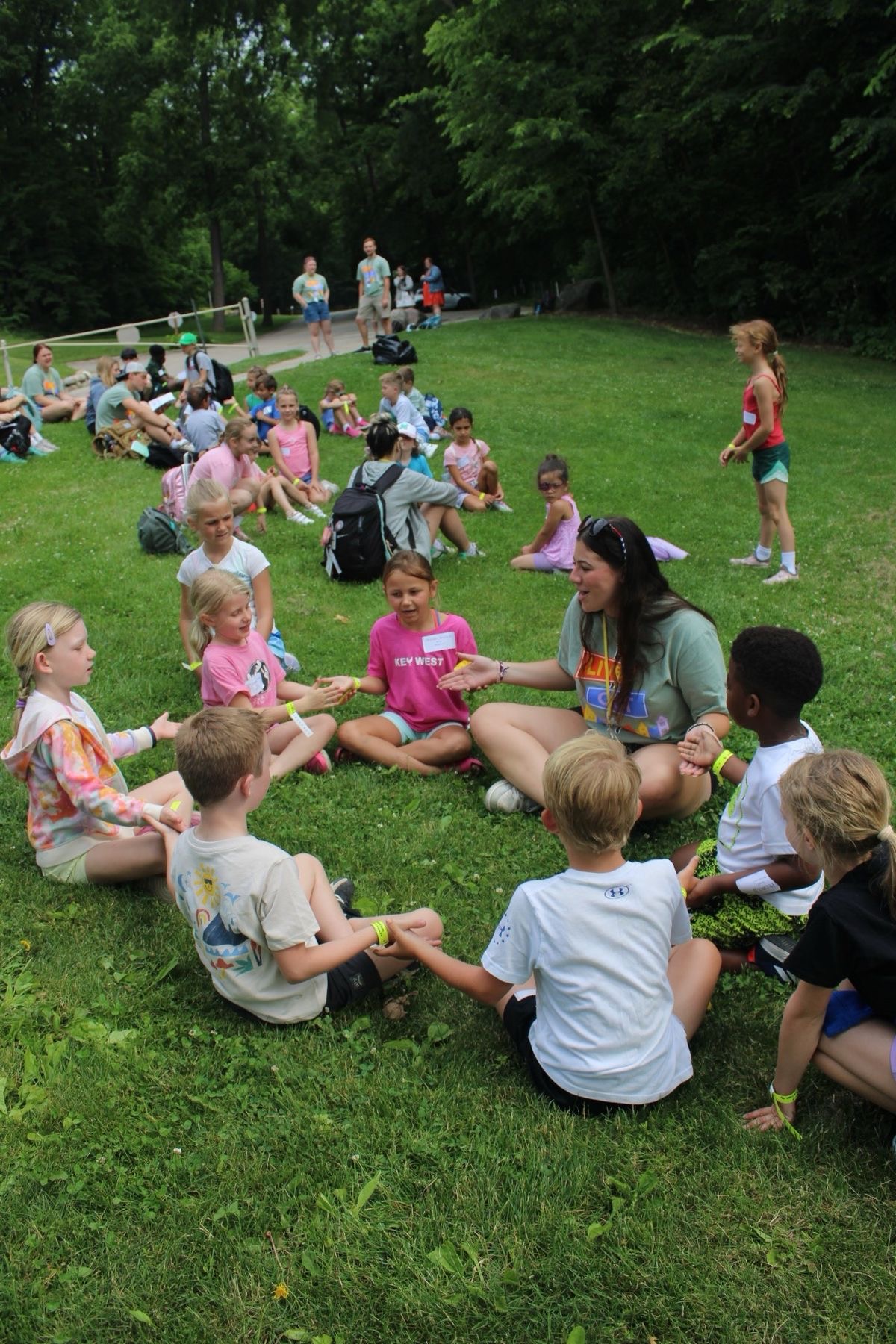 A caregiver leading a circle-time activity with a group of children on the grass